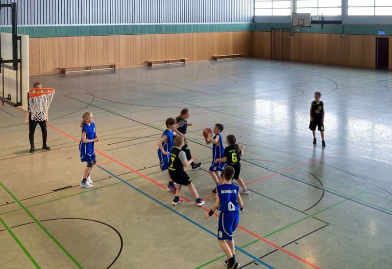 Eine Gruppe von Kindern spielt Basketball in einer Turnhalle.
